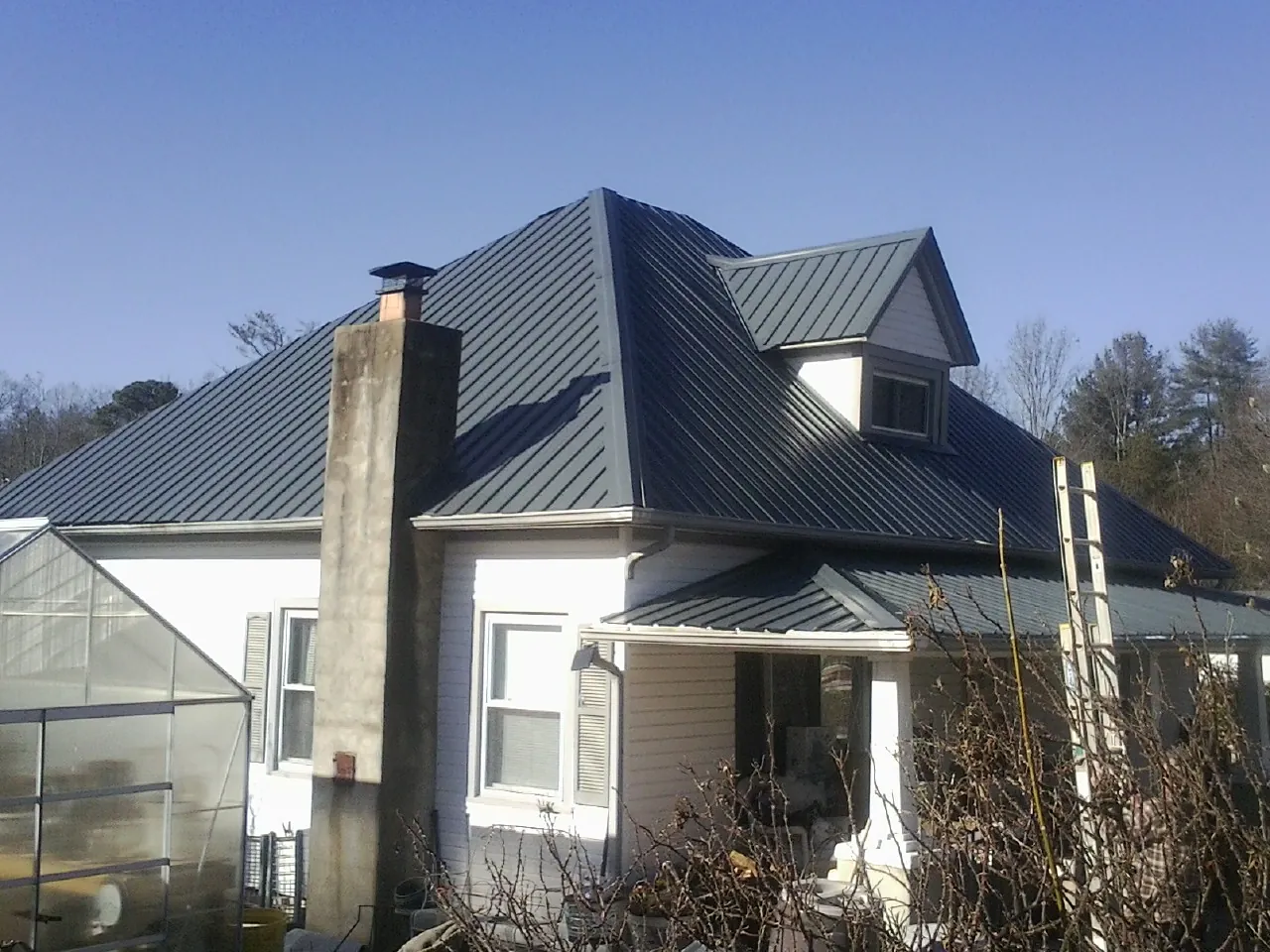Dark blue standing seam metal roof on a white farmhouse with dormer — Slate & Tile Roof Repair by Roofing Brothers in Bassett
