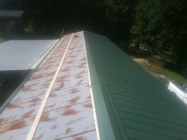Old rusted panels beside newly installed green metal roofing — Wind Damage Roof Repair by Roofing Brothers in Bassett