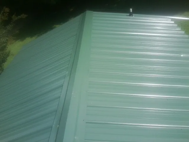 New green metal panels meeting at the ridge of a roof — Flat Roof Repair work by our crew in Bassett