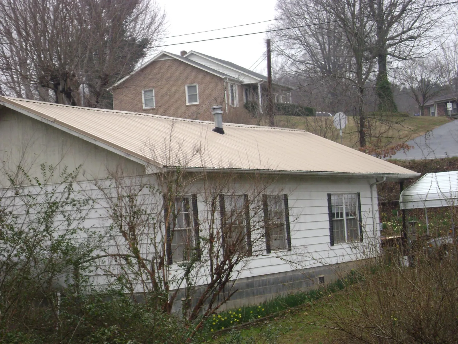 Tan metal roof on a white sided house set into a hillside — Commercial Roofing by Roofing Brothers in Bassett